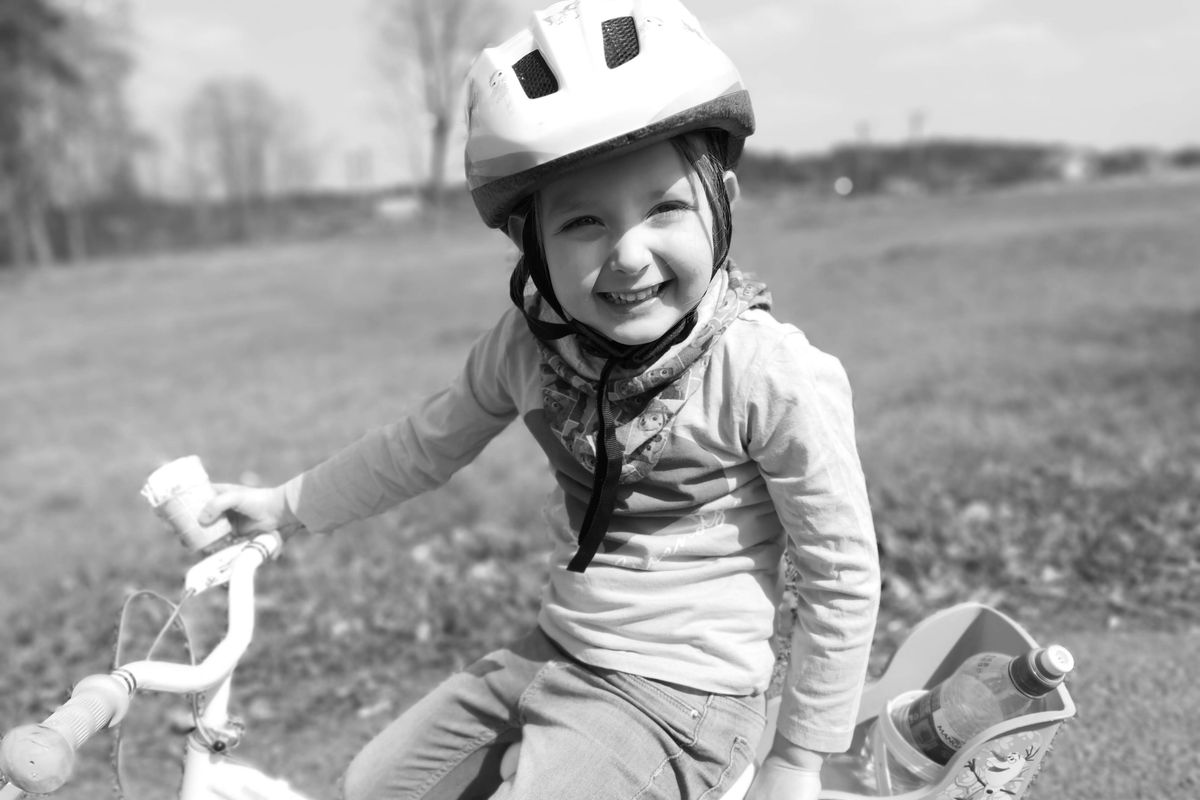 Young child smiling while riding a bike wearing a properly fastened white bike helmet