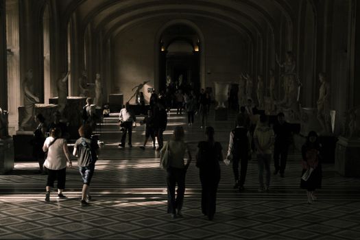 Visitors explore a classical hallway adorned with sculptures in a Paris museum, creating a moody ambiance.
