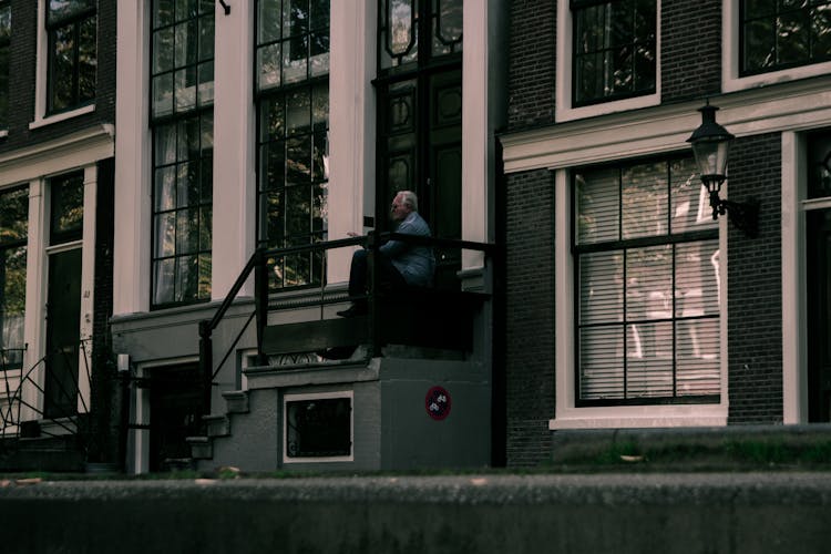 An Elderly Man Sitting On The Building Stoop