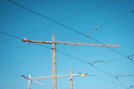 Tower cranes stand tall with intersecting power lines under a clear blue sky.