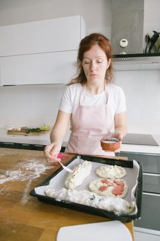 A woman in an apron is preparing dough on a wooden table in a contemporary kitchen.