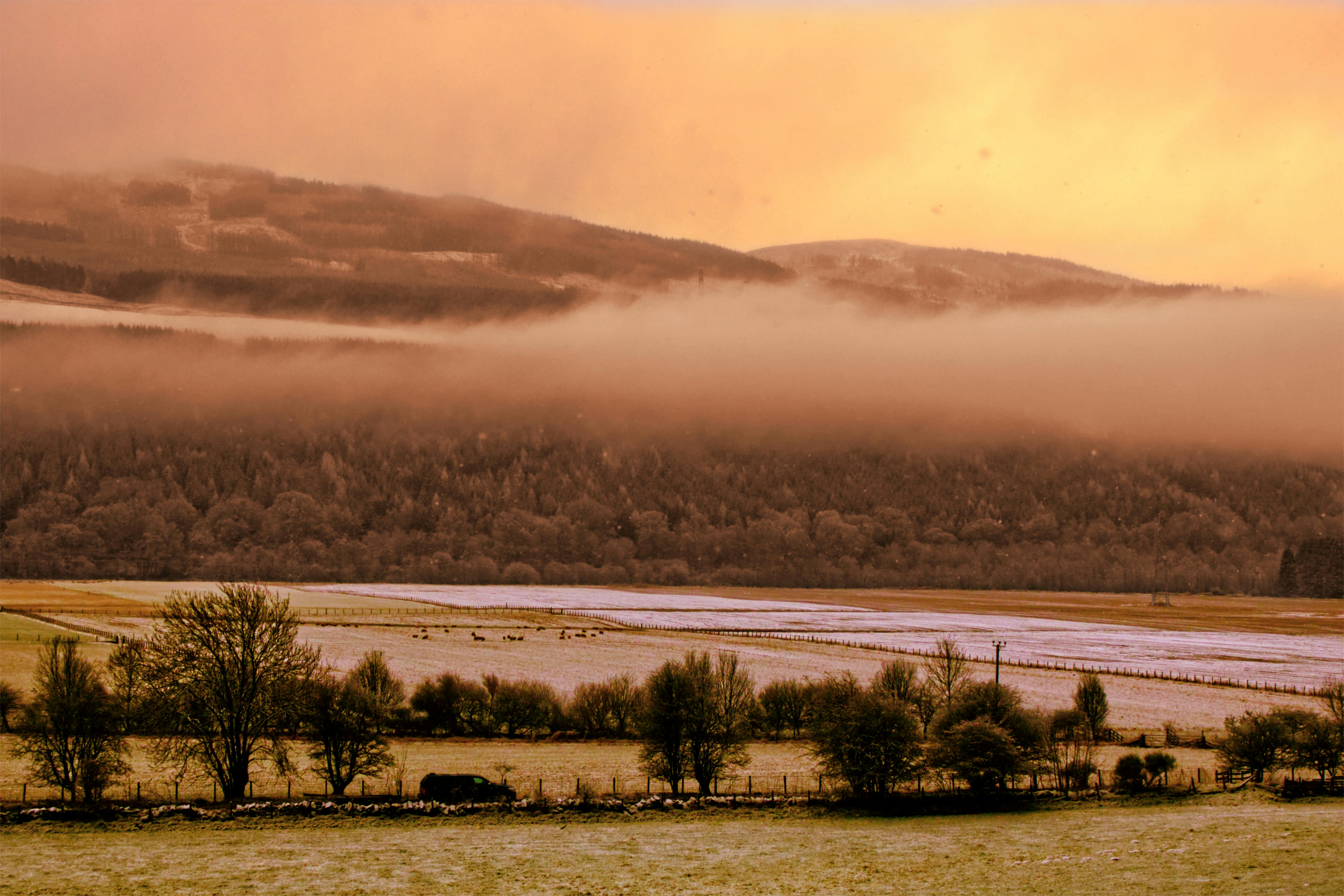 Explore this misty morning landscape in Pitlochry, Scotland, with an orange sky and serene countryside views.