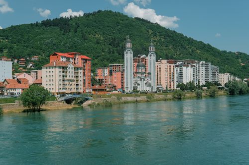 Free Scenic view of residential buildings and church by a river with green hills in the background. Stock Photo