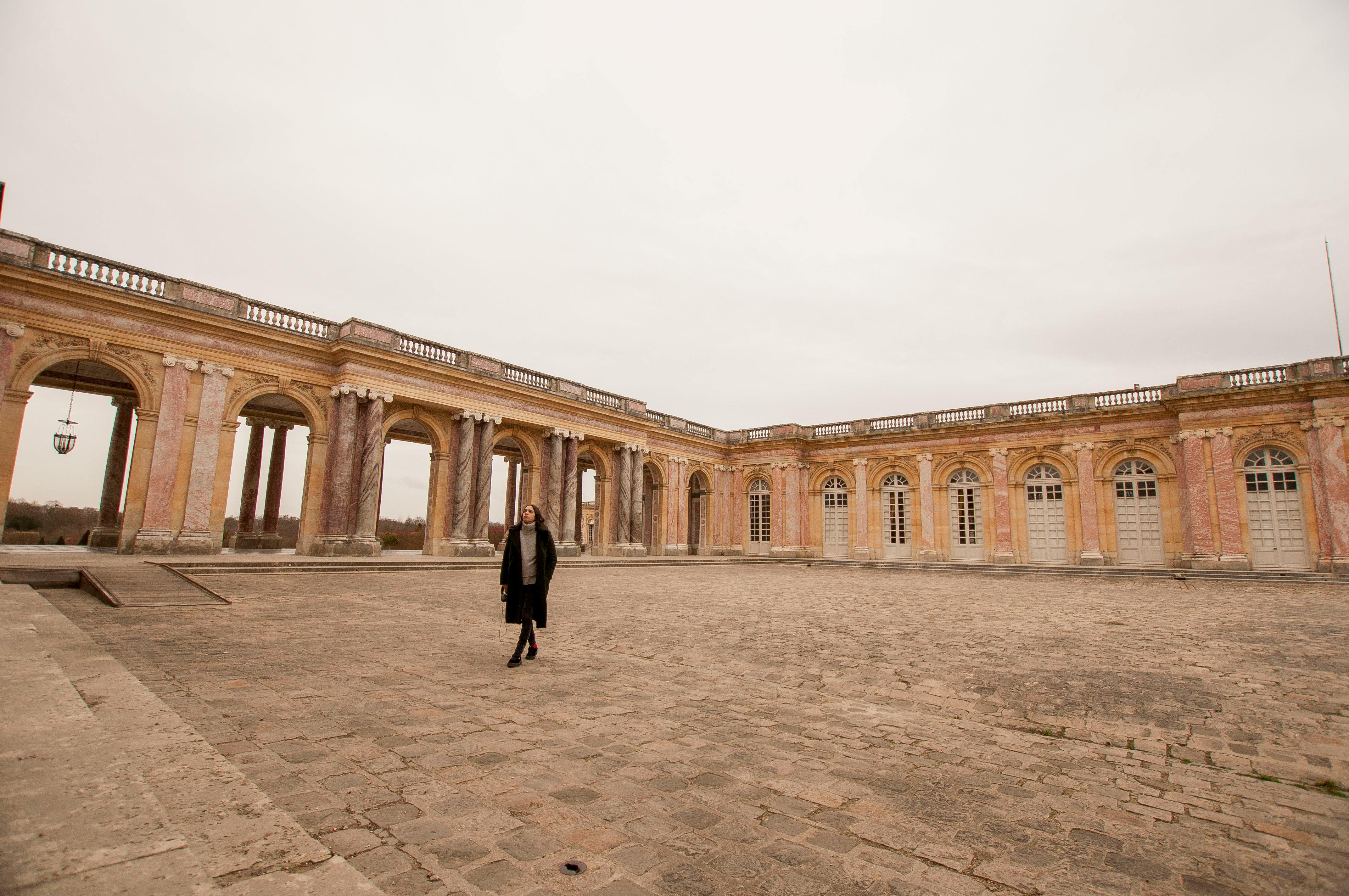 A woman walks through the historic courtyard of the Grand Trianon Palace in Versailles, France.