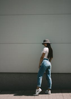 Fashionable woman in denim poses against a wall, showcasing style and urban fashion.