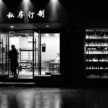 Black and white photo of a restaurant entrance at night with lit signage and glass doors.