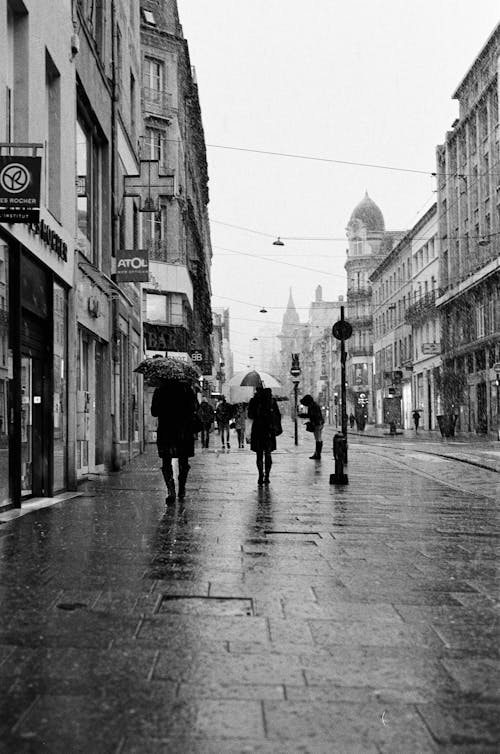 Grayscale Photo of People Walking on Street Between Buildings