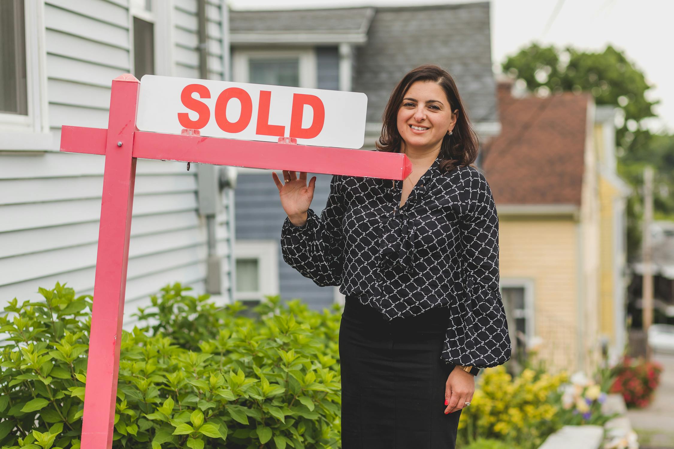 A woman near a sold sign thinking about ways to find your real estate niche.
