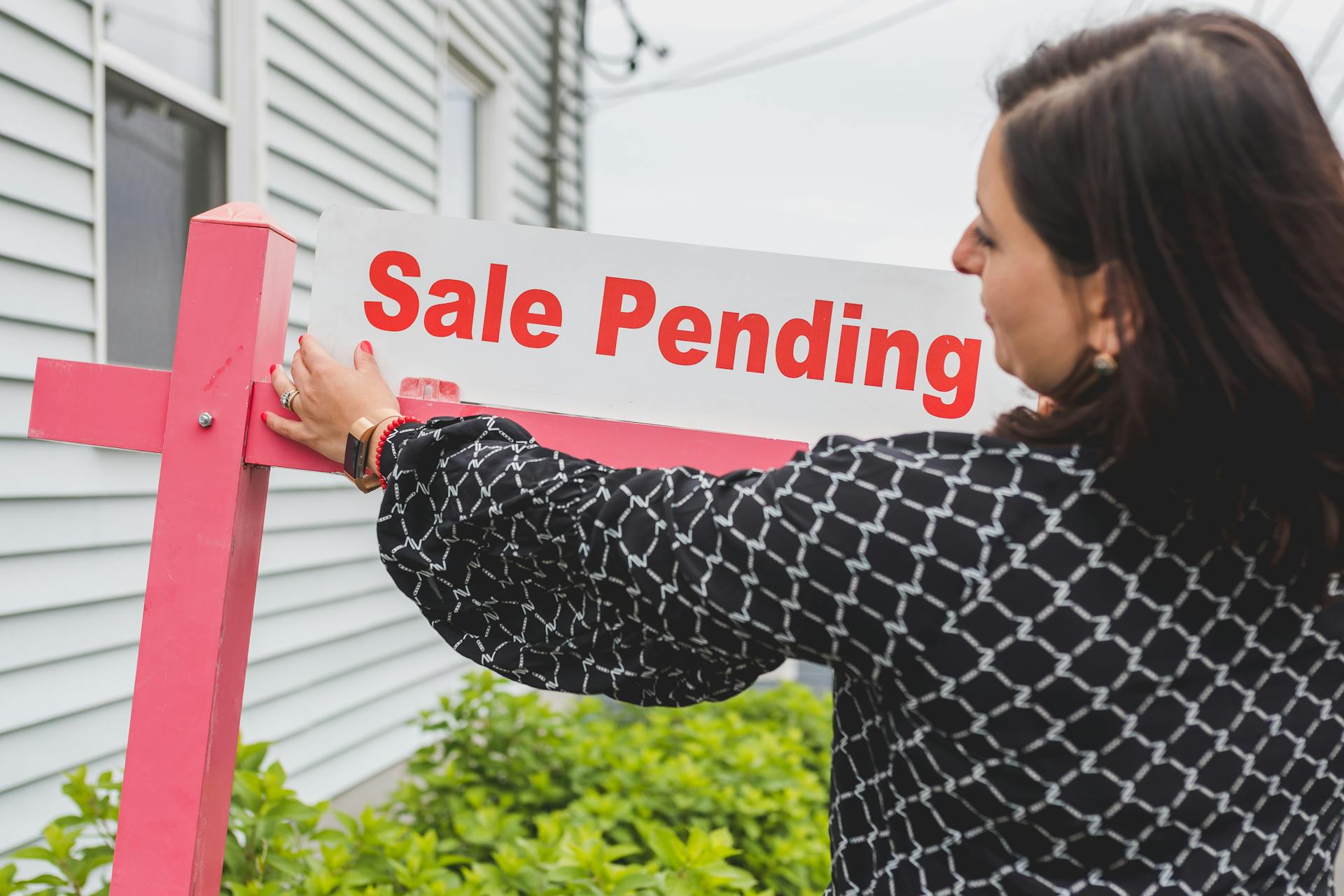 Female realtor adjusts sale pending sign on a property, indicating an upcoming sale closure.