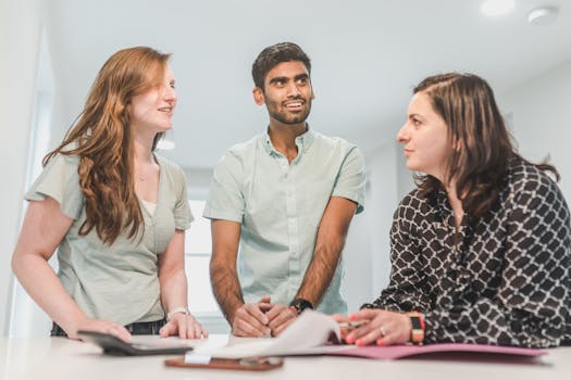 Three diverse adults conversing happily about real estate in a bright indoor setting.