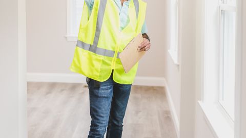 Construction inspector in a safety vest and hard hat examining an empty house interior.