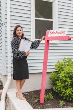 Confident female realtor standing next to a Sale Pending sign outside a house, showcasing success.