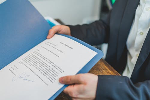 Person Holding and Showing a Printed Document on Blue Folder