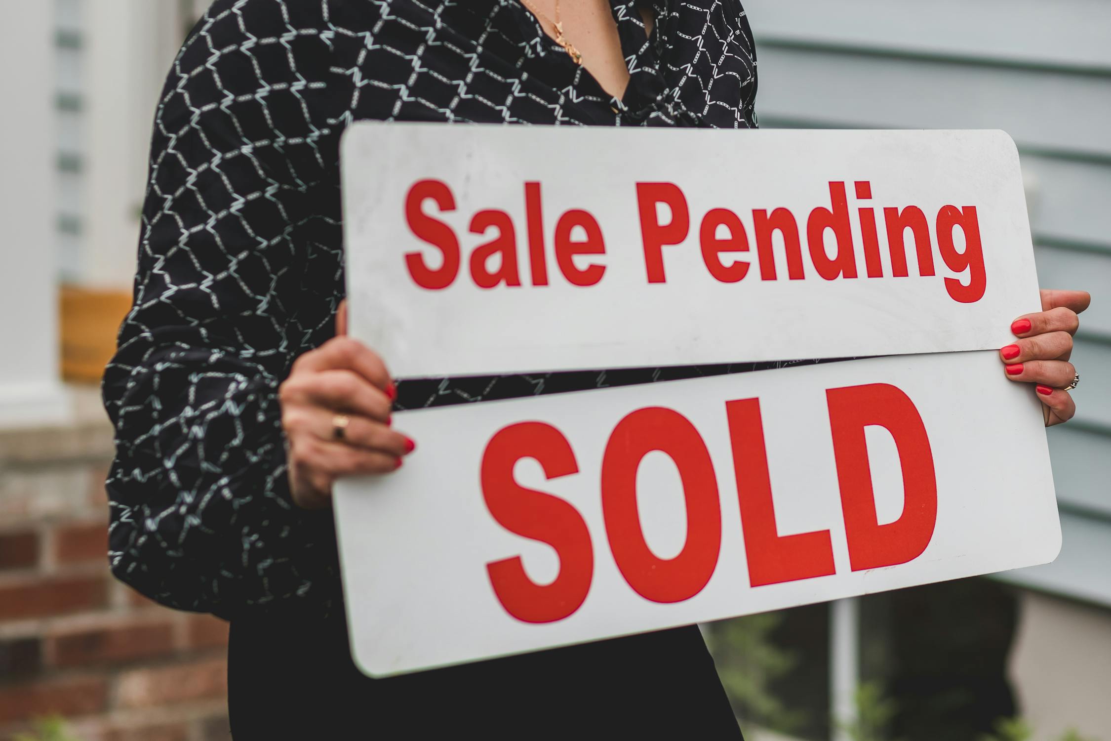 A person holding signs saying “Sale Pending” and “Sold”