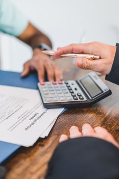 Hands working with a calculator and documents at a business meeting.