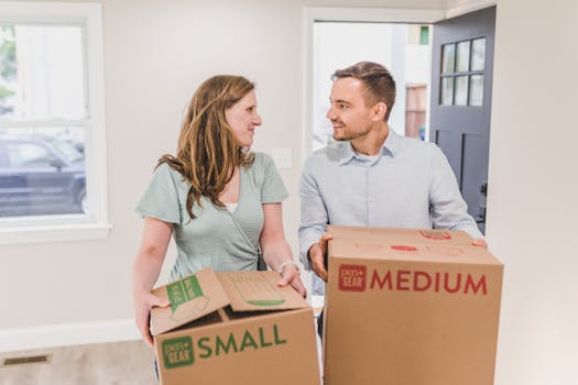 A smiling couple carries moving boxes into their new home, symbolizing a fresh start.