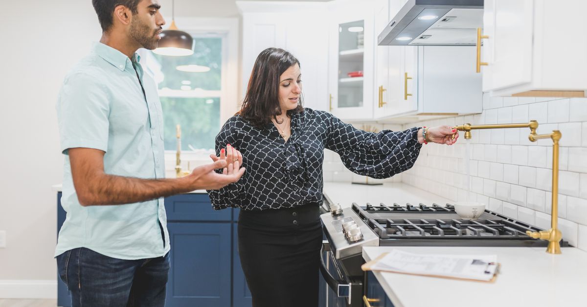 Real estate agent showing a modern kitchen interior with brass fixtures to a client.