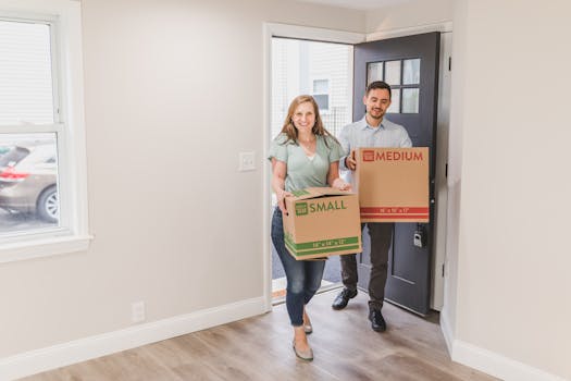 A joyful couple carrying boxes into their new home, symbolizing a fresh start.
