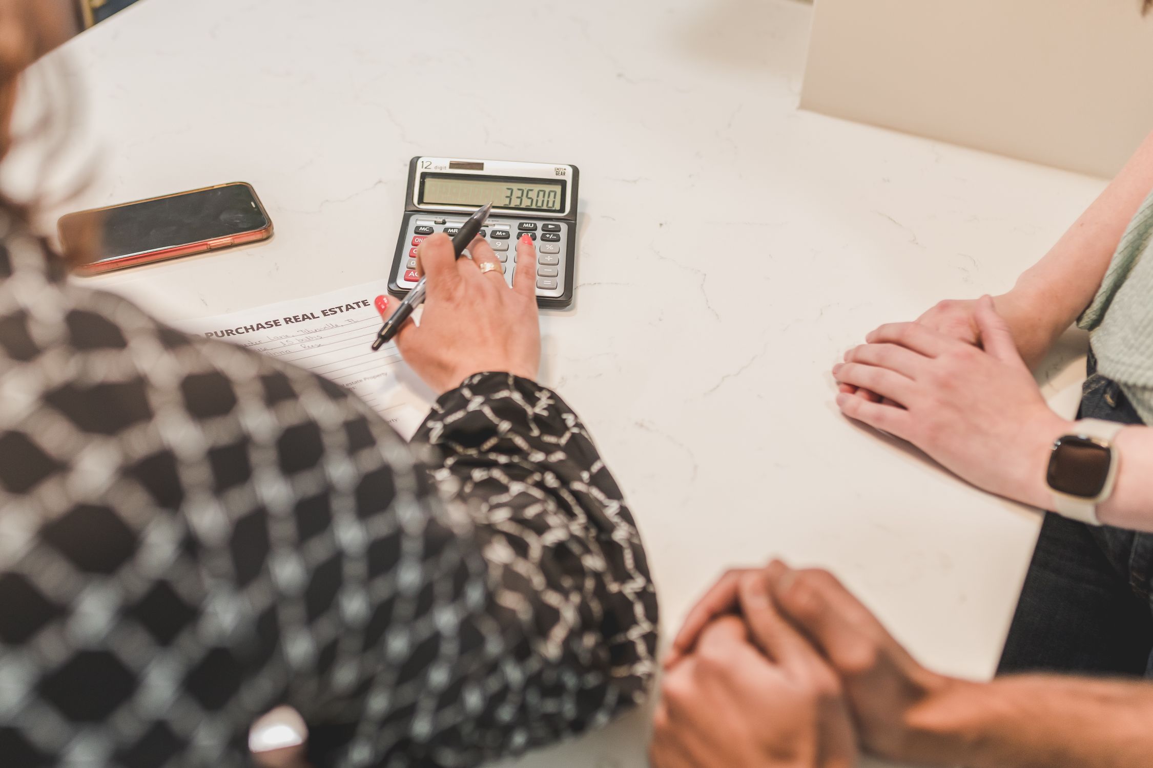 Real estate investor using a calculator with financing documents on desk