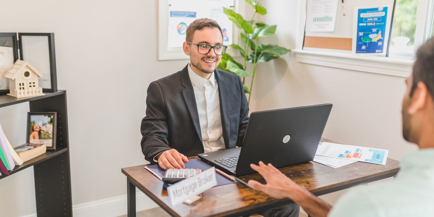 Mortgage broker in an office meeting with a client, utilizing a laptop.