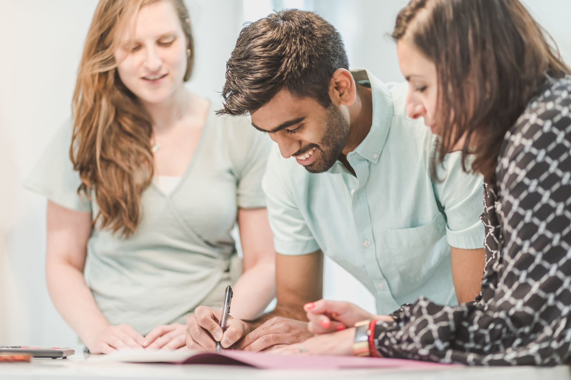 Diverse group of young professionals collaborating and signing documents together.