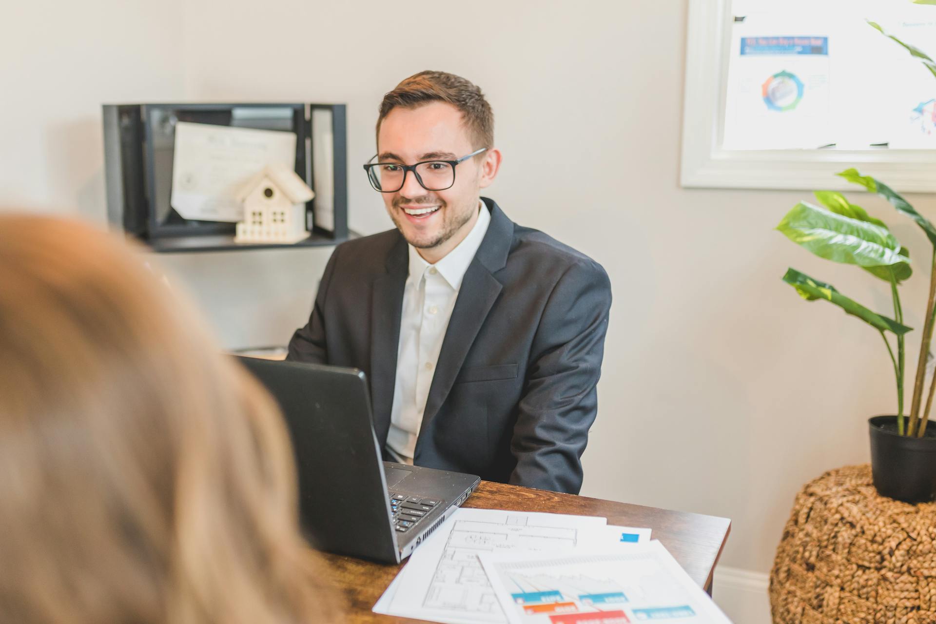 A smiling businessman works at his desk with a laptop and documents in a modern office.