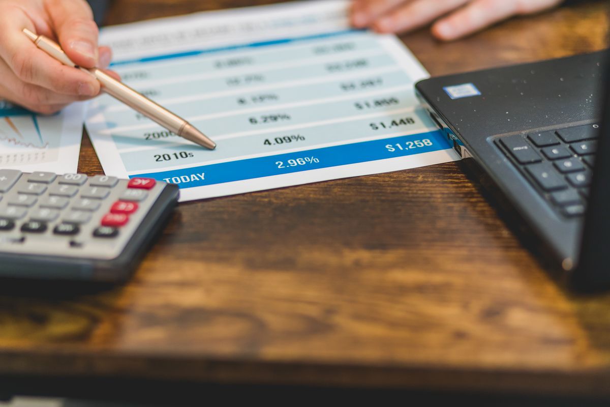 Hand using a calculator with a laptop and financial paperwork on a desk