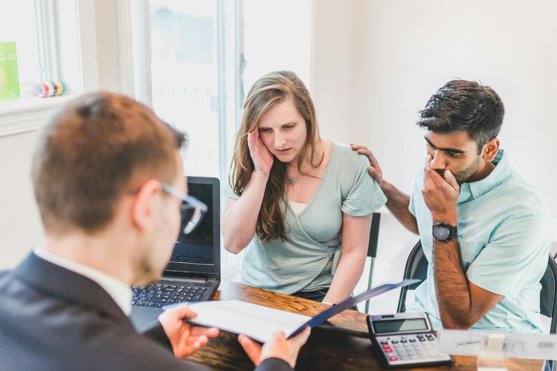 A worried couple consults with a real estate agent about home buying processes.