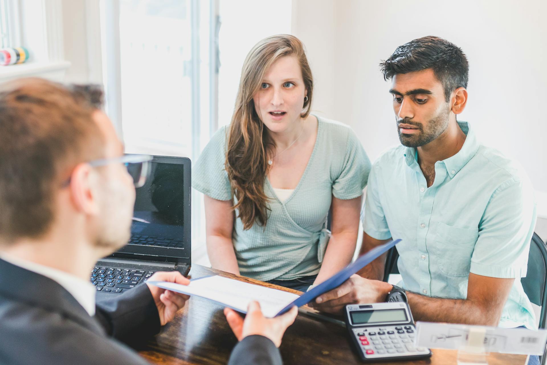 A young couple discusses home buying options with a real estate agent indoors.