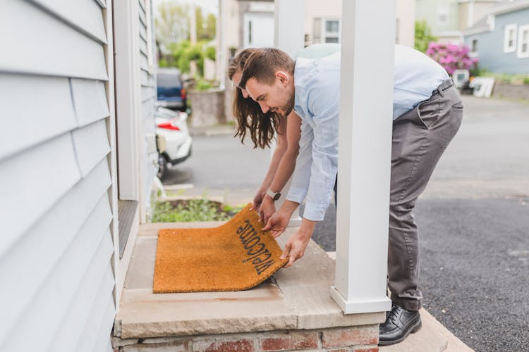 A Couple Putting A Welcome Mat At The Entrance Of Their House