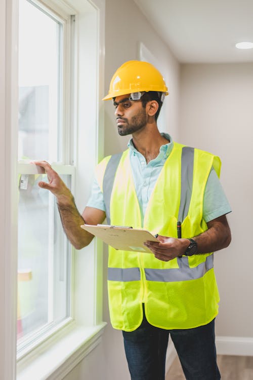 Free A Bearded Man in Safety Vest Looking at the Window while Holding a Clipboard Stock Photo