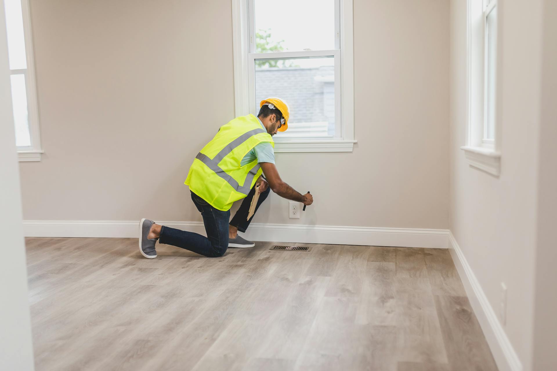 A home inspector in high visibility vest examines an electrical outlet in a modern room.