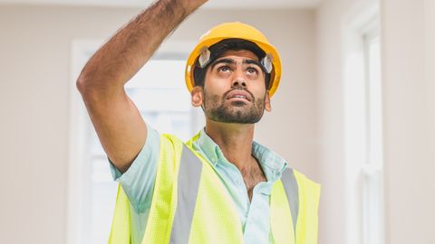 A construction worker inspecting a room while wearing a hardhat and safety vest indoors.