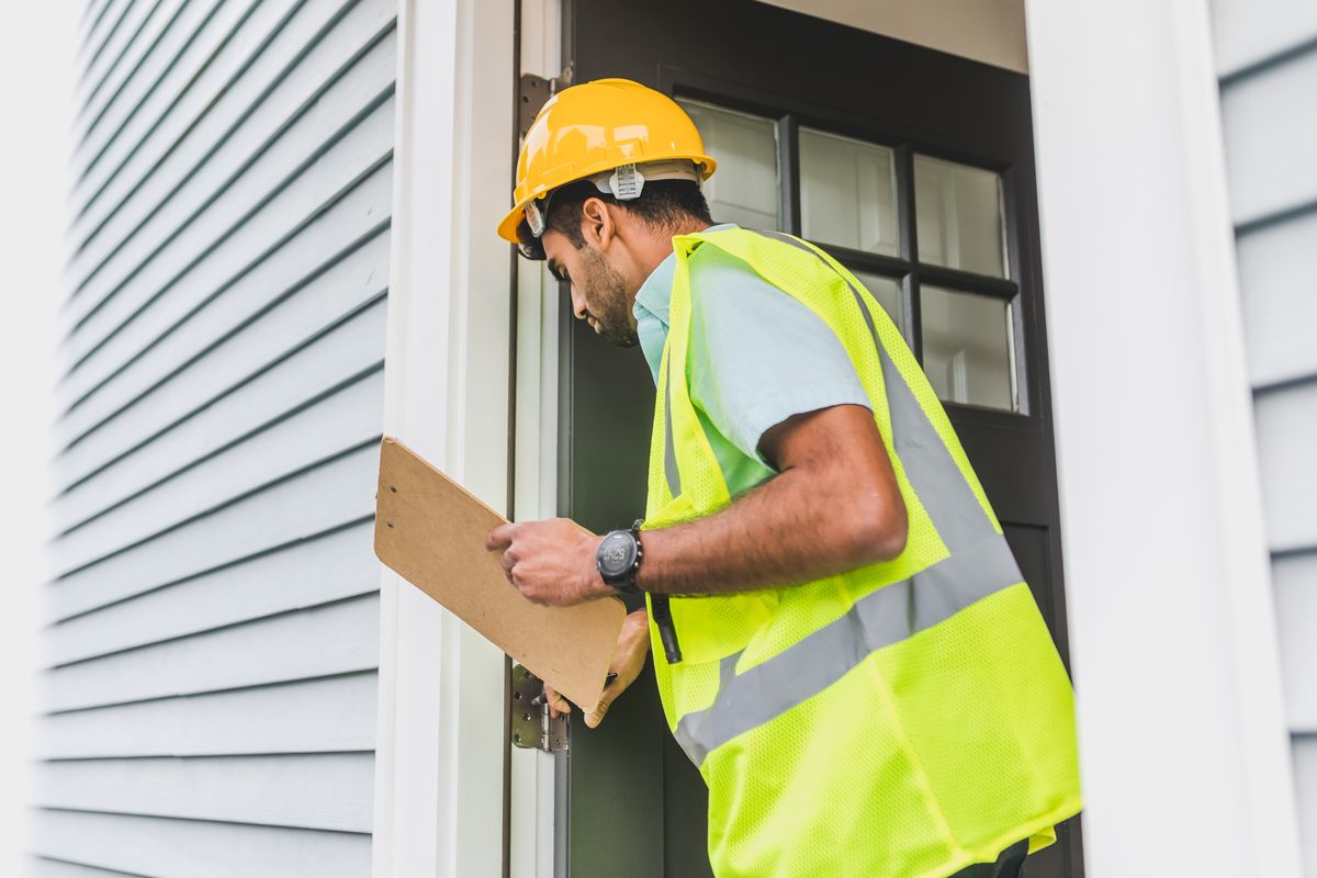 A property inspector in a hard hat conducting an outdoor inspection with a clipboard, documenting a roof scope
