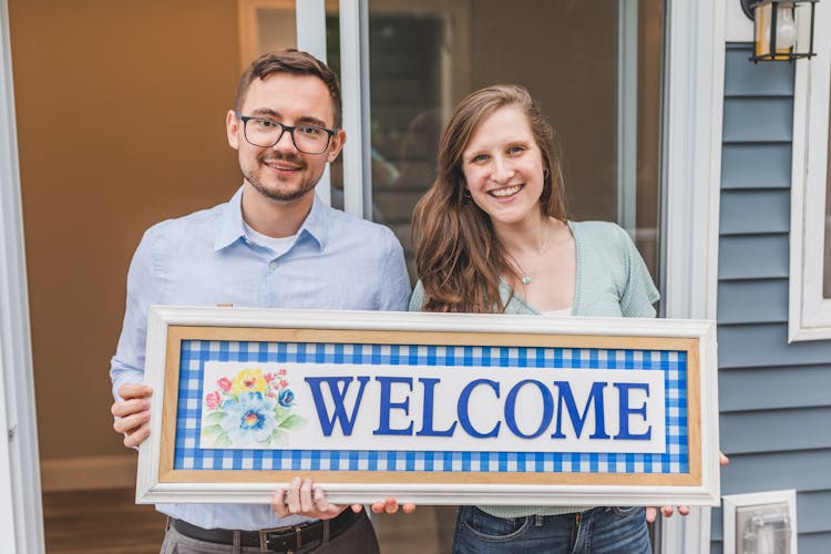 Couple Holding A Wooden Welcome Sign