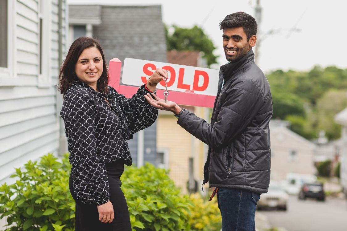 new home buyers holding a key near a sold sign outside a house