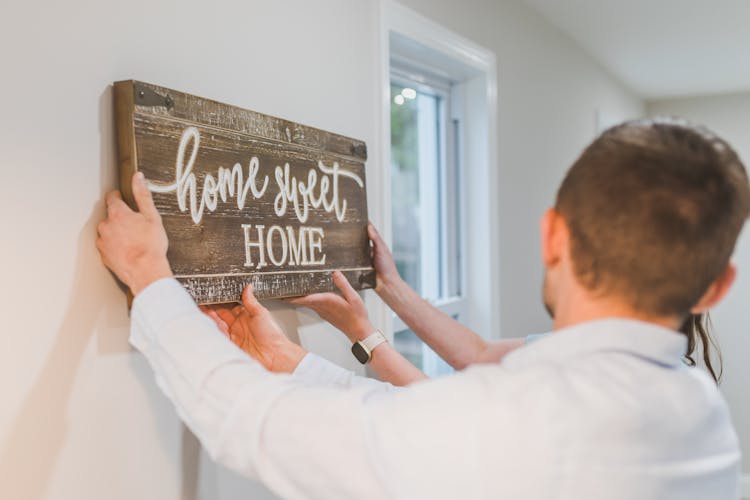 Couple Placing A Wooden Home Sweet Home Sign On Wall