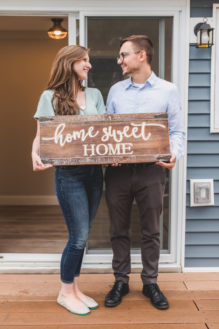 Happy Couple Standing Face To Face And Holding A Home Sweet Home Wooden Signage