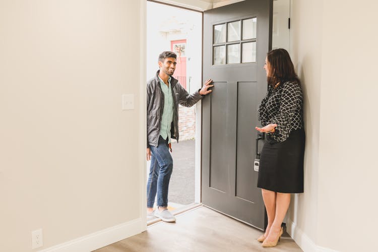 Real Estate Agent In Black Printed Blouse Welcoming A Client  Inside A For Sale House