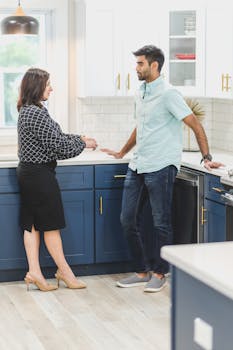 Two adults conversing in a stylish kitchen, featuring blue cabinets and a bright atmosphere.