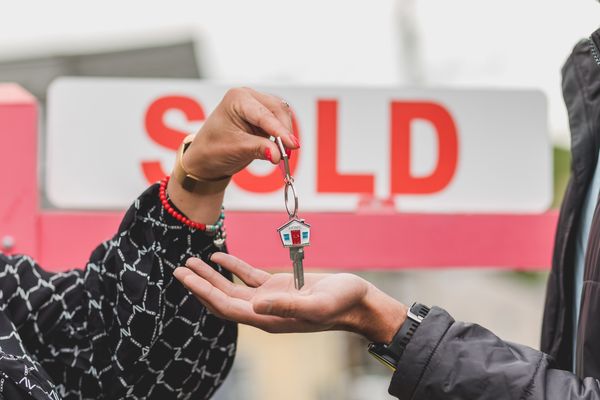 House keys being handed over in front of a sold sign after a home sale