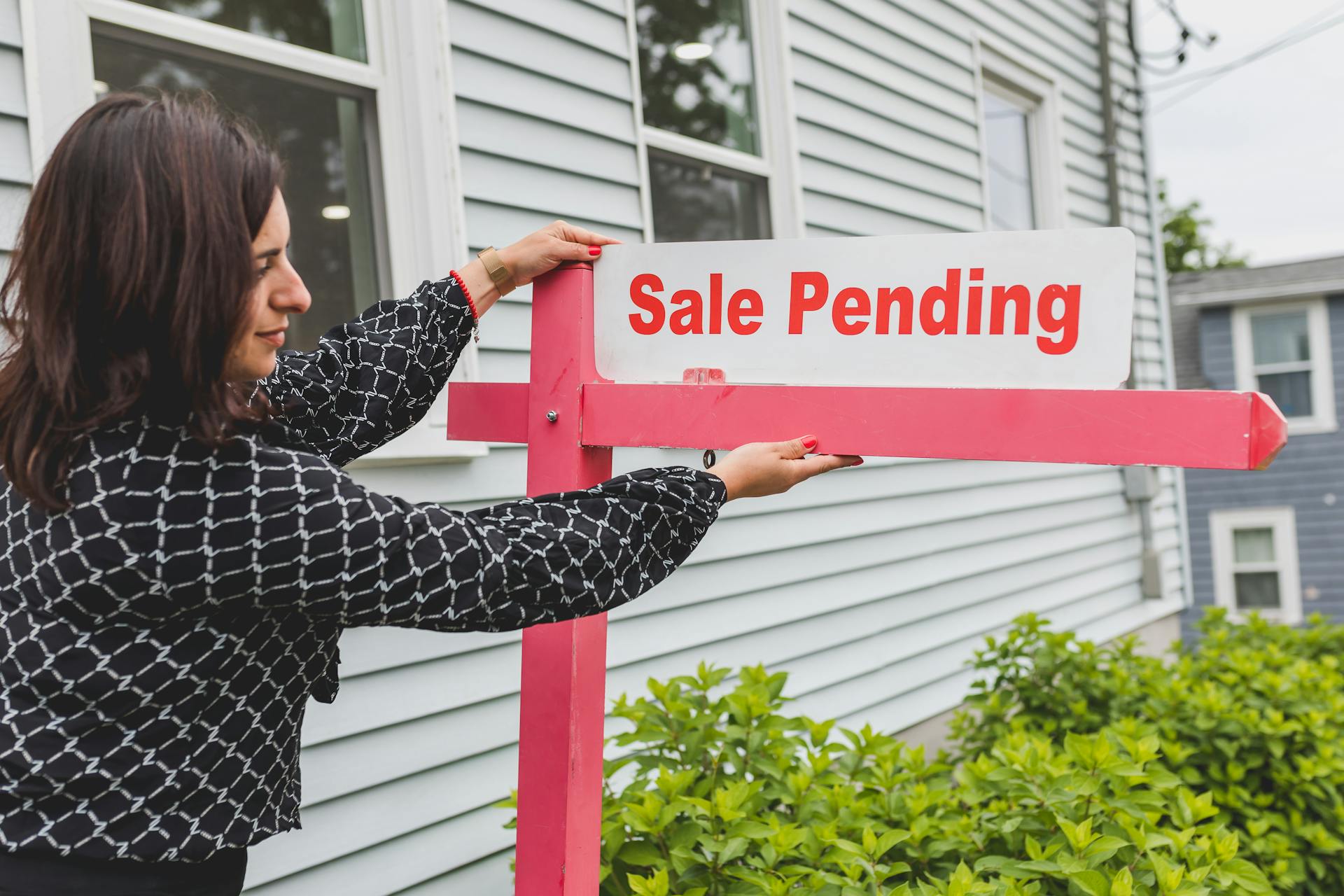 A realtor adjusting a sale pending sign outside a house for sale.