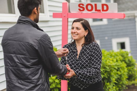 Real estate agent handing keys to a new homeowner with a 'Sold' sign in the background.