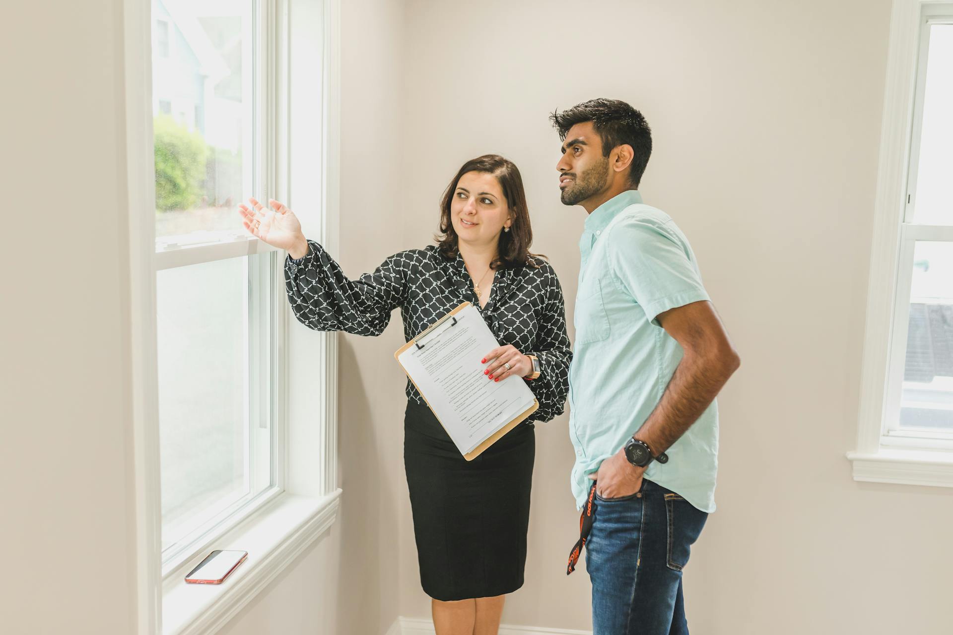 A real estate agent discusses property details with a client indoors, highlighting the view through large windows.