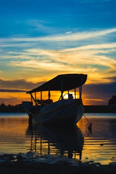 A serene silhouette of a boat during sunset, reflecting vibrant colors over calm waters.