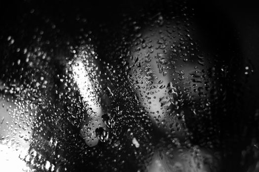 Glistening water droplets on a glass surface, creating a blurred abstract pattern in black and white.