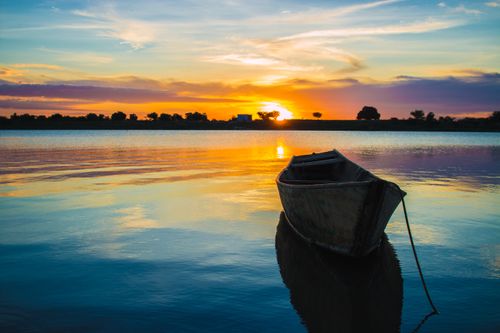 Free A wooden boat floats on calm waters at sunset, capturing a serene and colorful landscape. Stock Photo