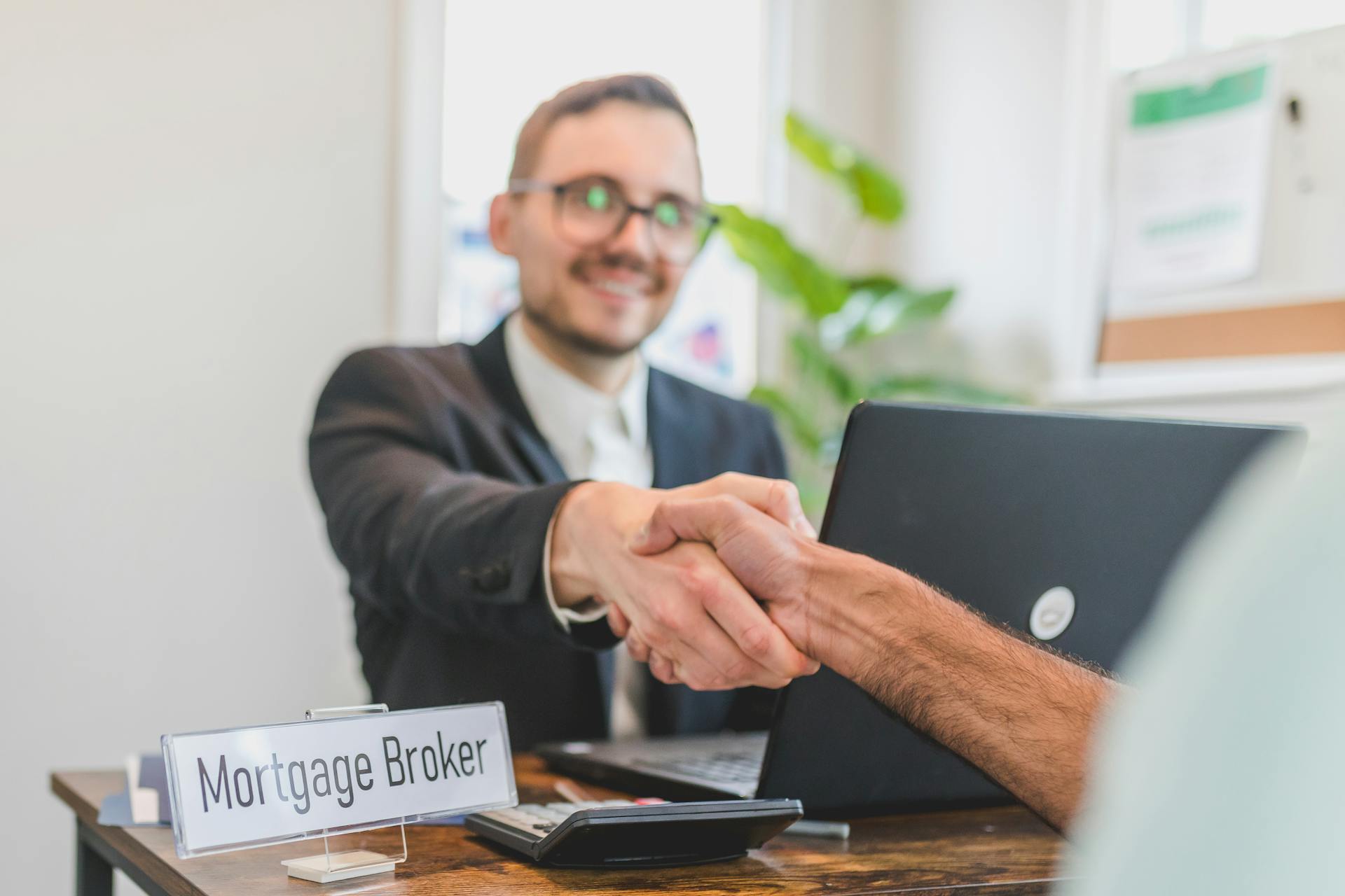 Mortgage broker and client sealing a deal with a handshake in a bright, modern office.