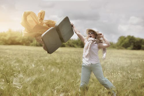 A Happy Woman Walking on the Field while Holding Her Suitcase