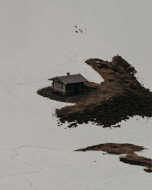 A solitary cabin on barren ground surrounded by snow, depicting winter isolation.
